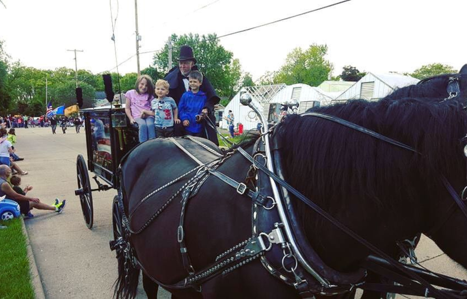 Rodger Cavanaugh leading a dignified funeral procession with a horse-drawn hearse carrying a casket draped in the American flag, accompanied by children paying tribute.