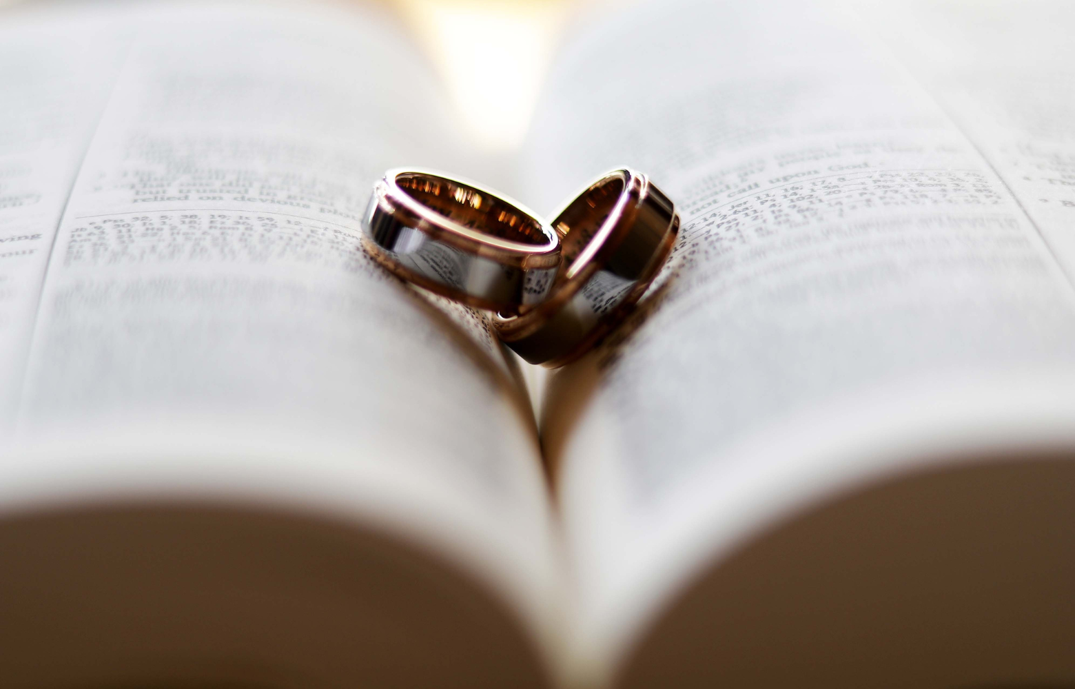 A Bible with two wedding rings placed on top, symbolizing the meaningful celebrations of weddings, vow renewals, and other cherished matrimonial events hosted by Cavanaugh Carriages.