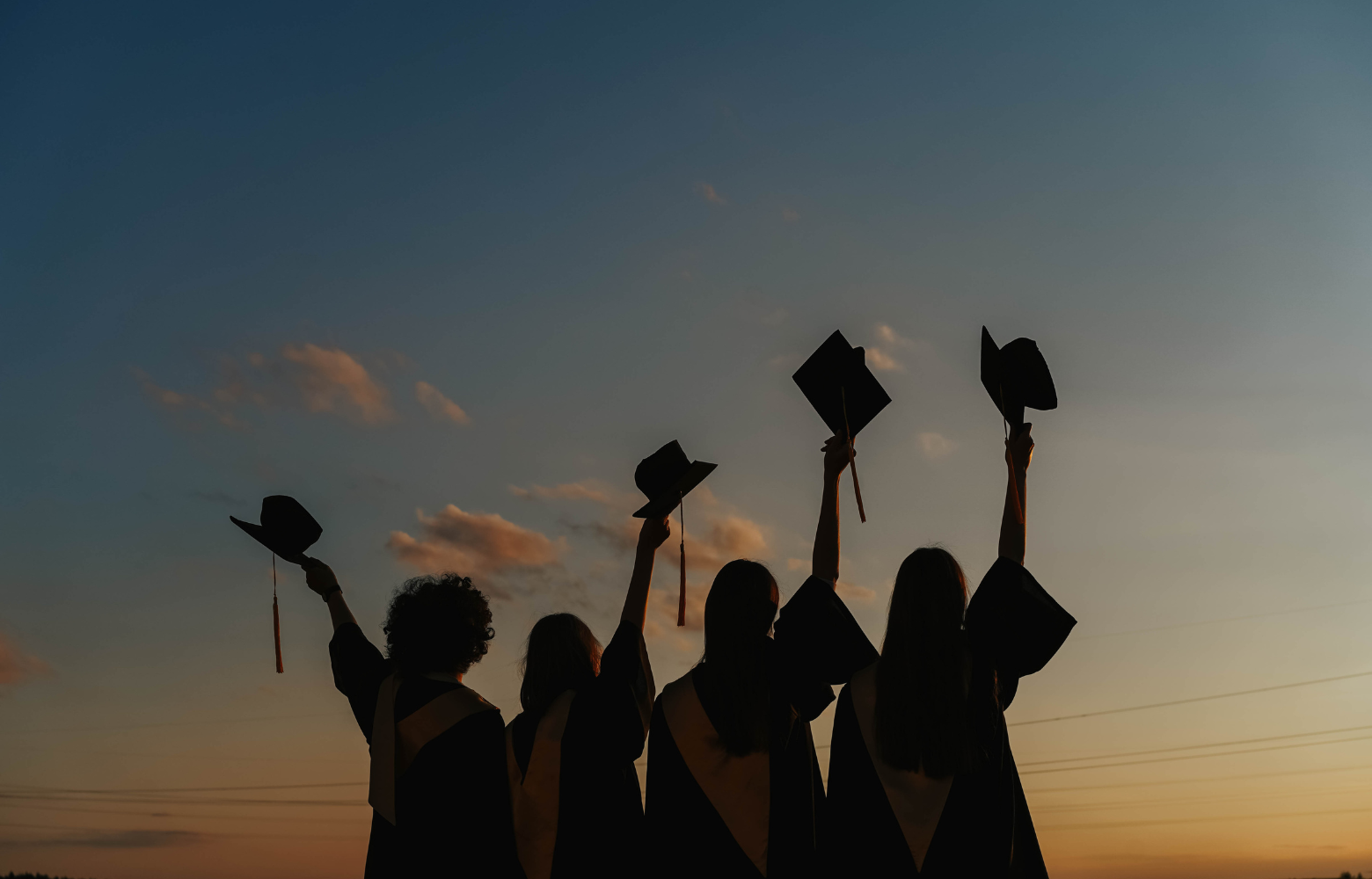 Graduates dressed in their caps and gowns, celebrating their achievement by raising their hats toward a sunset-lit sky, symbolizing milestone moments and special occasion services at Cavanaugh Carriages.